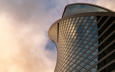 Curved modern skyscraper against cloudy sky.
